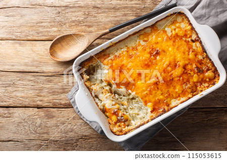 Homemade Cheesy Hashbrown Casserole with Potatoes and Cream closeup in the baking dish on the wooden table. Horizontal top view 115053615