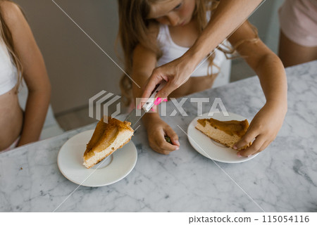 Mother puts a piece of apple pie on her children daughters plate for breakfast Mother puts a piece of apple pie on her children daughters plate for breakfast 115054116