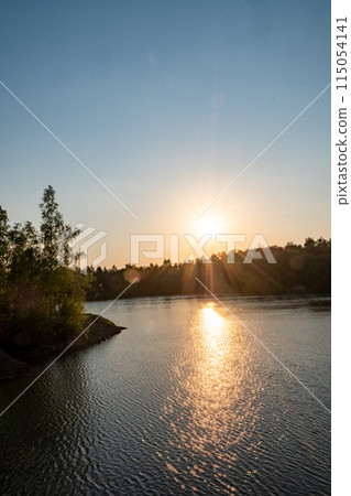 The sun sets over a tranquil lake, framed by a backdrop of trees The sun sets over a tranquil lake, framed by a backdrop of trees 115054141