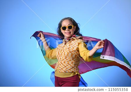 Older lady holding a rainbow flag on blue background LGBT, human rights, freedom and equality concept Older lady holding a rainbow flag on blue background LGBT, human rights, freedom and equality concept 115055358