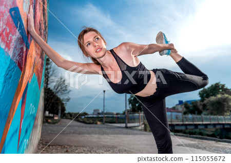 Young woman doing gymnastics on the street. Young woman doing sport exercise against colorful wall on city street. 115055672