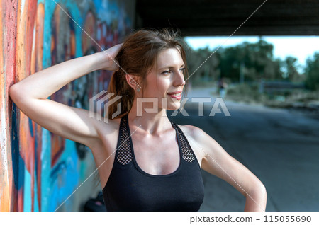 Young woman resting after doing gymnastics on the street. Portrait of fit and sporty young woman doing stretching in city. Young woman resting after doing gymnastics on the street. Portrait of fit and sporty young woman doing stretching in city. 115055690