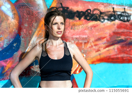 Young woman resting after doing gymnastics on the street. Portrait of fit and sporty young woman doing stretching in city. 115055691