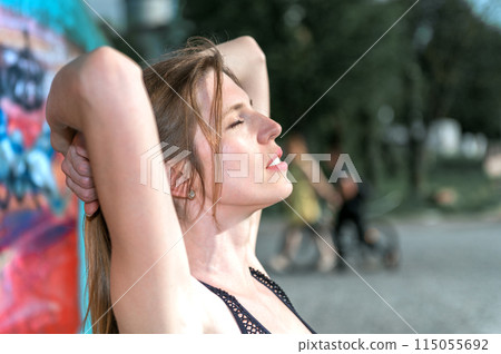 Young woman resting after doing gymnastics on the street. Portrait of fit and sporty young woman doing stretching in city. Young woman resting after doing gymnastics on the street. Portrait of fit and sporty young woman doing stretching in city. 115055692