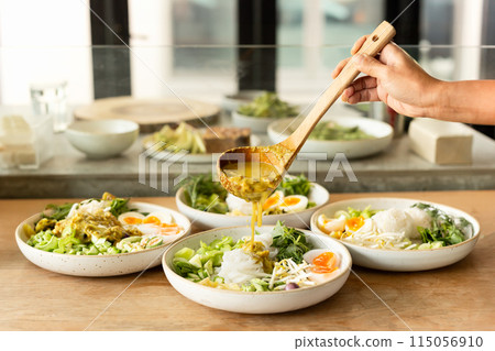 Woman hand pouring sauce into Thai rice noodles dish on table. Woman hand pouring sauce into Thai rice noodles dish on table. 115056910