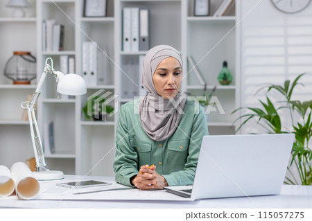 Woman in hijab designer working in home office, architect using laptop at work, studying technical assignment online, serious and concentrated reading. Woman in hijab designer working in home office, architect using laptop at work, studying technical assignment online, serious and concentrated reading. 115057275