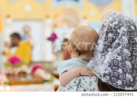 Unrecognised rear view of woman in white headscarf holding the baby against icons in a church. Selective focus. 115057441