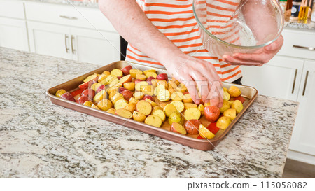 In a modern, white kitchen, a young man is engrossed in dinner preparations. His current endeavor includes arranging seasoned rainbow potatoes on a baking sheet, a meticulous step towards a In a modern, white kitchen, a young man is engrossed in dinner preparations. His current endeavor includes arranging seasoned rainbow potatoes on a baking sheet, a meticulous step towards a 115058082