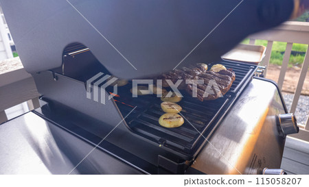 The outdoor two-burner gas grill is put to good use, sizzling with the sound and aroma of ribeye steaks and onion rings being perfectly cooked. 115058207