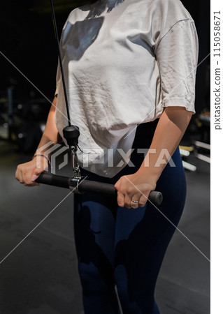 A woman is in the gym holding a barbell with her hand A woman is in the gym holding a barbell with her hand 115058671