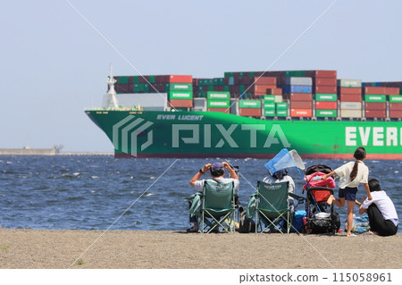 A family watches a cargo ship sailing offshore from the beach 115058961