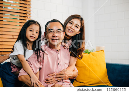 In their modern home a smiling family shares a sweet moment on the sofa highlighting togetherness. Parents daughters and siblings bond laugh and embrace in a joyful family portrait. In their modern home a smiling family shares a sweet moment on the sofa highlighting togetherness. Parents daughters and siblings bond laugh and embrace in a joyful family portrait. 115060355