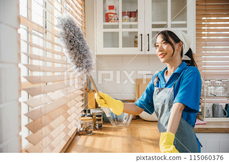 Portrait of a smiling Asian woman cleaning window blinds. She stands duster in hand enjoying her routine housework. Modern cleaning occupation ensuring hygiene and cleanliness. whisk 115060376