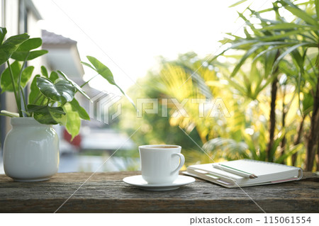 White coffee cup on wooden tray and notebook and Philodendron plant on wooden table under sunlight 115061554
