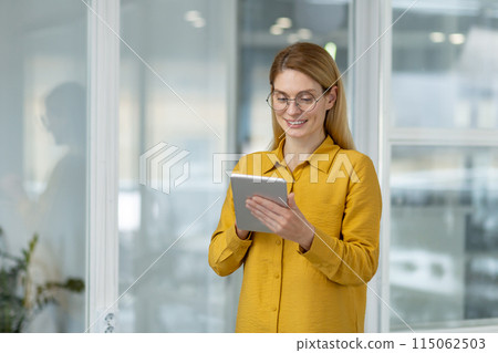 Smiling woman using a tablet in a bright, modern office environment. Ideal for business, technology, and workplace concepts. Smiling woman using a tablet in a bright, modern office environment. Ideal for business, technology, and workplace concepts. 115062503