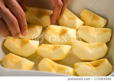 Woman putting apple pieces on ceramic baking sheet to bake, hands close-up. 115064086