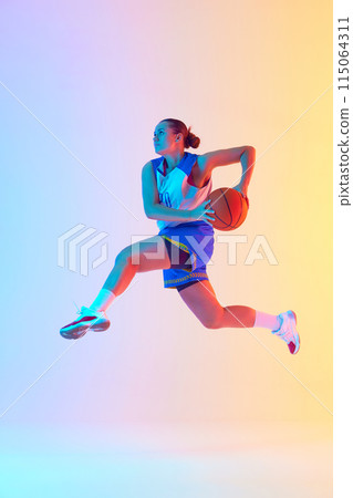 Female basketball player in blue jersey preparing to make perfect slam dunk leaping in mid-air in neon light against gradient studio background. Female basketball player in blue jersey preparing to make perfect slam dunk leaping in mid-air in neon light against gradient studio background. 115064311