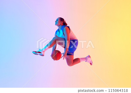 Dynamic photo of young basketball player leaping to make powerful slam dunk in neon light against gradient studio background. 115064318