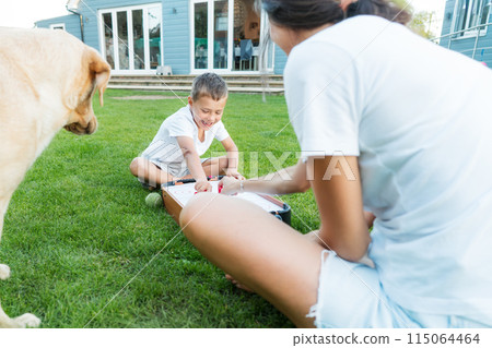 Joyful little boy and his mother are playing portable air hockey in the garden. Fun Playing Games in Backyard Lawn on Summer Day. Happy family time with pet together. Solo parenting. Active childhood. Joyful little boy and his mother are playing portable air hockey in the garden. Fun Playing Games in Backyard Lawn on Summer Day. Happy family time with pet together. Solo parenting. Active childhood. 115064464