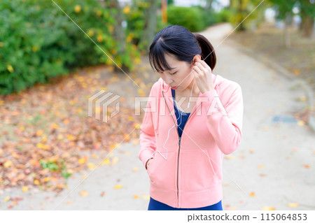 A young woman walking while listening to music with wired earphones Body makeup Running wear A young woman walking while listening to music with wired earphones Body makeup Running wear 115064853