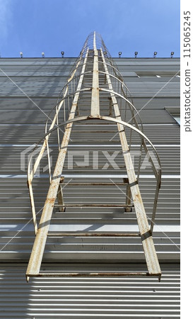 External fire metal ladder on gray wall of building, evacuation vertical ladder with safety railings External fire metal ladder on gray wall of building, evacuation vertical ladder with safety railings 115065245
