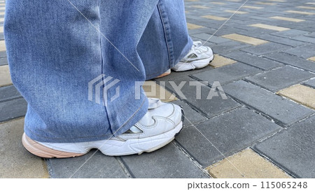 Female legs in light modern bell-bottom jeans in white leather sneakers, modern streetwear style Female legs in light modern bell-bottom jeans in white leather sneakers, modern streetwear style 115065248