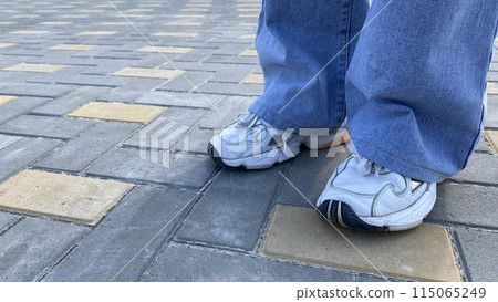 Legs of a girl in wide blue jeans and white sneakers, modern street fashion for pants Legs of a girl in wide blue jeans and white sneakers, modern street fashion for pants 115065249