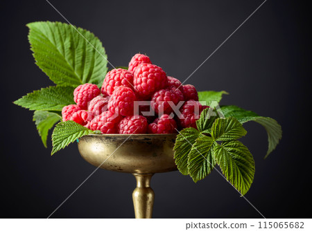Fresh raspberries with leaves in an old brass dish. Fresh raspberries with leaves in an old brass dish. 115065682