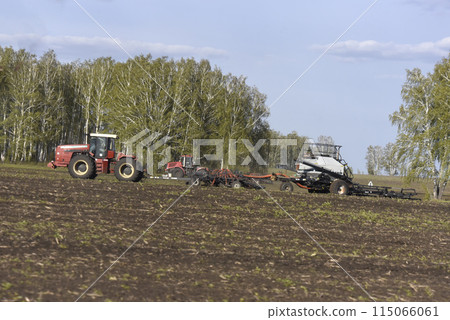 Agricultural machines for sowing grain in the field. Red tractors in the sowing campaign. Agricultural machines for sowing grain in the field. Red tractors in the sowing campaign. 115066061