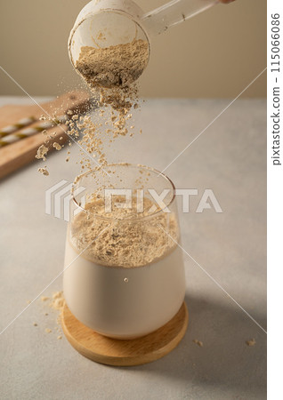 Pouring protein powder in glass with milkshake. Pouring protein powder in glass with milkshake. 115066086