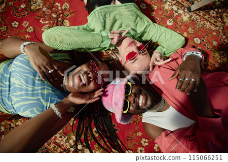 Top view closeup of three trendy young people lying on ornate carpet and smiling at camera Top view closeup of three trendy young people lying on ornate carpet and smiling at camera 115066251