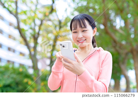 年輕女性邊走邊看智慧型手機、身體化妝、跑步服 年輕女性邊走邊看智慧型手機、身體化妝、跑步服 115066279