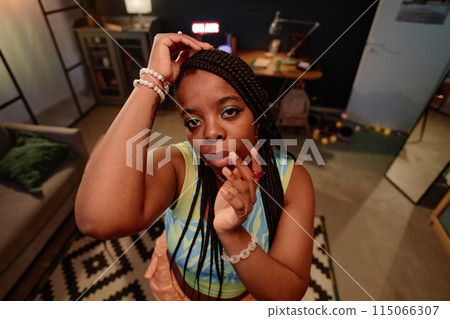 High angle view at trendy Black young woman dancing indoors and looking at camera recording videos for social media or livestream 115066307