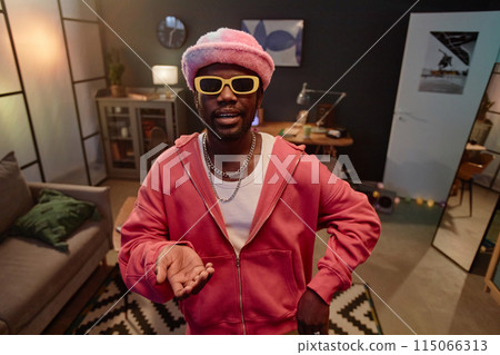 Waist up portrait of African American man wearing pink outfit with sunglasses recording livestream for social media indoors copy space 115066313