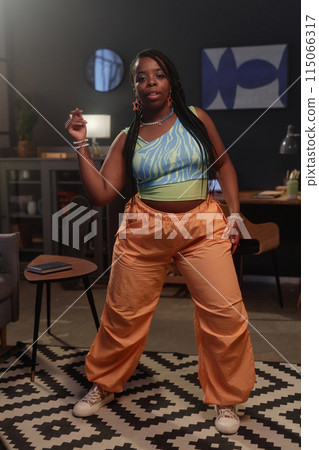 Vertical full length portrait of young Black woman dancing hip-hop style at home and recording videos for social media 115066317