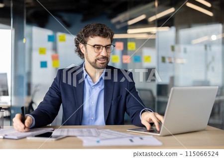 Serious focused businessman financier doing paperwork, accountant checking data from laptop and writing in paper tables, man in business suit experienced investor preparing report. 115066524