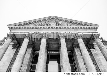 The monochrome facade of the Reichstag building, showcasing its iconic pillars and inscription: Dem Deutschen Volke. The seat of the German Bundestag, Berlin, Germany.. Black and white image. The monochrome facade of the Reichstag building, showcasing its iconic pillars and inscription: Dem Deutschen Volke. The seat of the German Bundestag, Berlin, Germany.. Black and white image. 115066945