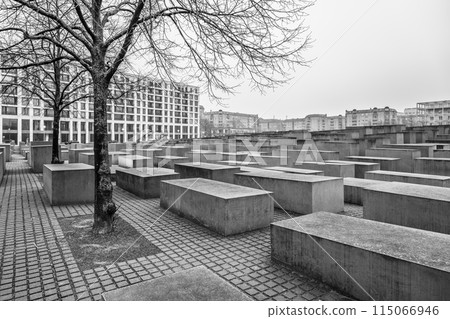 Barren trees and concrete stelae stand under a cloudy sky at the Holocaust Memorial in Berlin. Black and white image. 115066946
