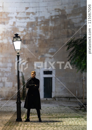 A man stands in front of a street lamp, looking at the camera A man stands in front of a street lamp, looking at the camera 115067006