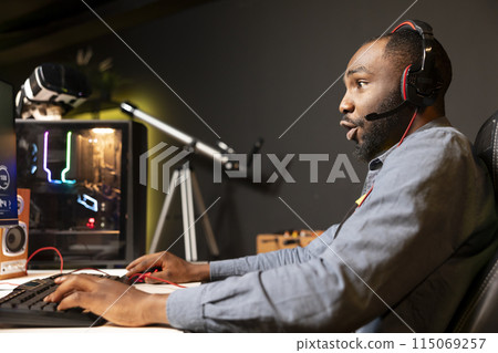 African american man wearing headphones while playing videogame at home, showing amazement emotion on face. Player in awe while enjoying game on computer, astonished by high quality graphics African american man wearing headphones while playing videogame at home, showing amazement emotion on face. Player in awe while enjoying game on computer, astonished by high quality graphics 115069257