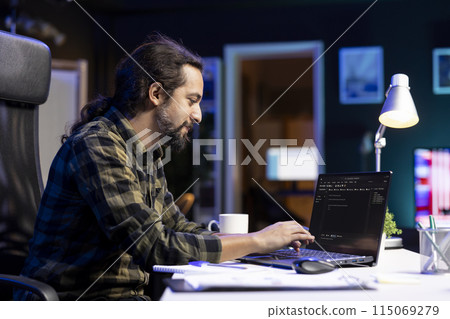 Male programmer works on his portable computer, managing the database and monitoring network for cyber security. Young man sitting at desk and using digital laptop for coding. 115069279