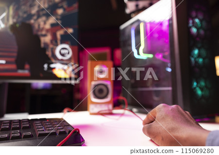 Gamer using keyboard and mouse to play FPS videogame on gaming PC tower with neon lit components. Man in apartment at night using high tech computer peripherals to defeat foes, close up 115069280