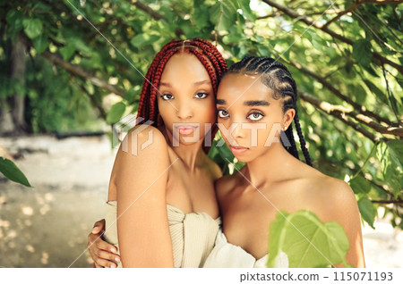 Fashion Close up outdoor portrait Beautiful young African American female couple with braids hair posing at sunny summer day green foliage. Cosmetology, perfect skin care, spa. Natural face treatment. 115071193