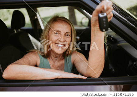 Senior woman sitting in new car outdoors holding keys, smiling, enjoying journey. Driving courses and life insurance. Retired people activity and road trip concept. Happy female client car dealership. 115071196