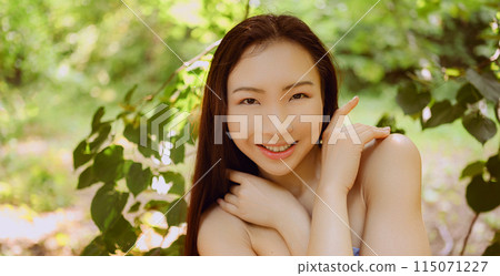 Close up outdoor portrait Beautiful young Chinese Asian woman perfect skin posing outside sunny summer day green foliage. Natural facial treatment. Cosmetology, skin care and spa. Fragnance concept. 115071227