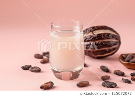 A translucent glass of cacao water, surrounded by raw cacao beans 115072072