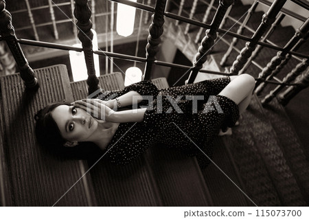 A woman in a black dress is laying on a staircase A woman in a black dress is laying on a staircase 115073700