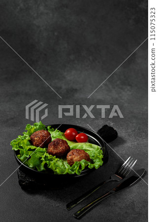 Fried cutlets on a lettuce leaf with tomato on a black background 115075323