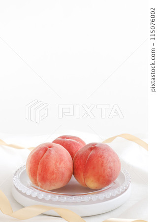 Delicious looking peaches served on a plate with gold ribbon and draped cloth on a white background 115076002
