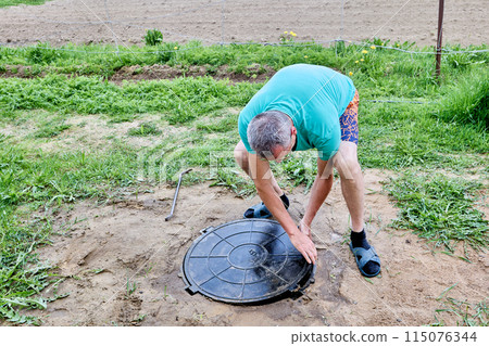 Man covers septic tank with manhole cover made of polymer composite materials. 115076344